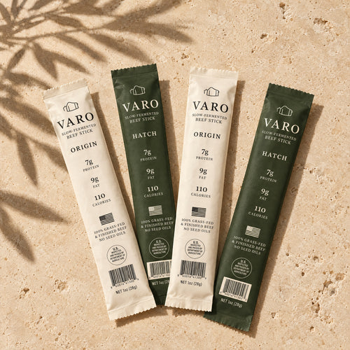Four wrapped VARO slow-fermented beef sticks, two ORIGIN and two HATCH, fanned on travertine