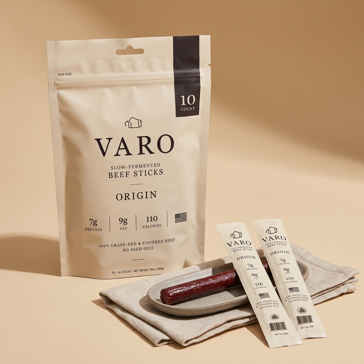 ORIGIN bag of VARO slow-fermented beef sticks with two wrapped sticks and an unwrapped stick on a plate and linen