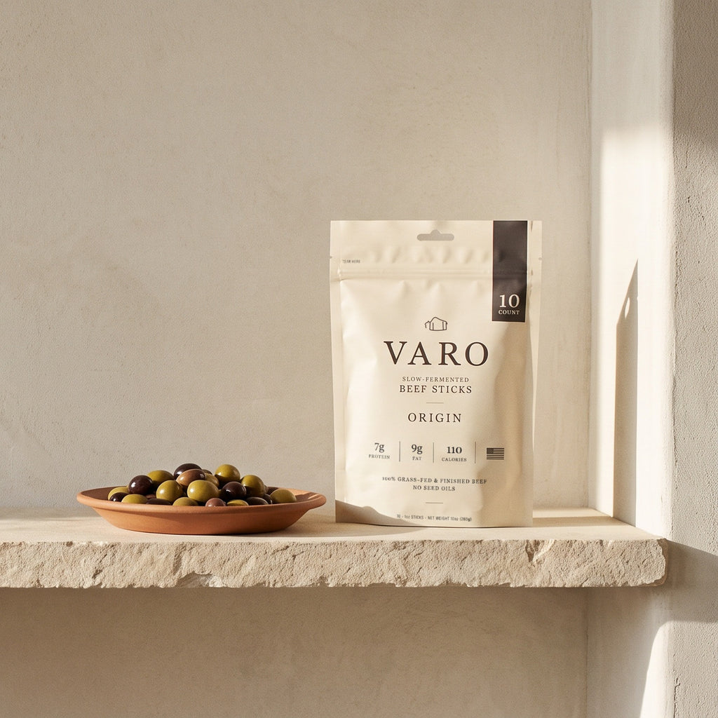 ORIGIN bag of VARO slow-fermented beef sticks on a stone shelf beside a terracotta dish of olives