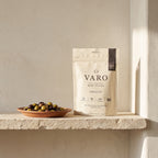 ORIGIN bag of VARO slow-fermented beef sticks on a stone shelf beside a terracotta dish of olives