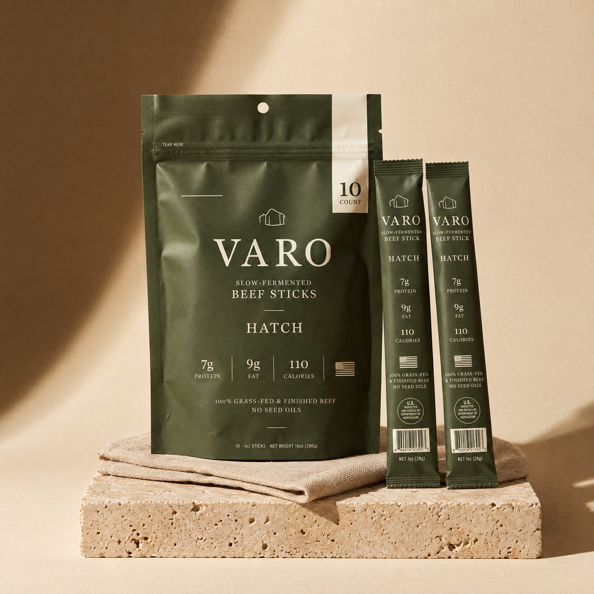 HATCH bag of VARO slow-fermented beef sticks with two wrapped HATCH sticks on travertine and linen